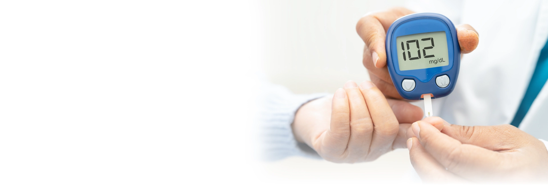 Header_Diabetologie_1920x650 Nahaufnahme einer Hand, die mithilfe eines Blutzuckermessgeräts den Blutzuckerwert einer anderen Person misst – auf dem Display ist ein Wert von 102 mg/dL zu sehen, symbolisiert Diabetesdiagnostik in der Arztpraxis.