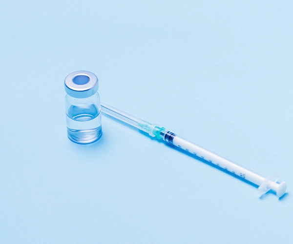 Impfung Nahaufnahme einer gefüllten Spritze neben einem kleinen Impf-Fläschchen auf hellblauem Hintergrund – symbolisiert Impfung oder Medikamentengabe.