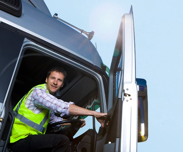 LKW-Fahrer Mann in Warnweste sitzt lächelnd in der geöffneten Fahrerkabine eines Lkw – symbolisiert Berufskraftfahrer und arbeitsmedizinische Untersuchung.