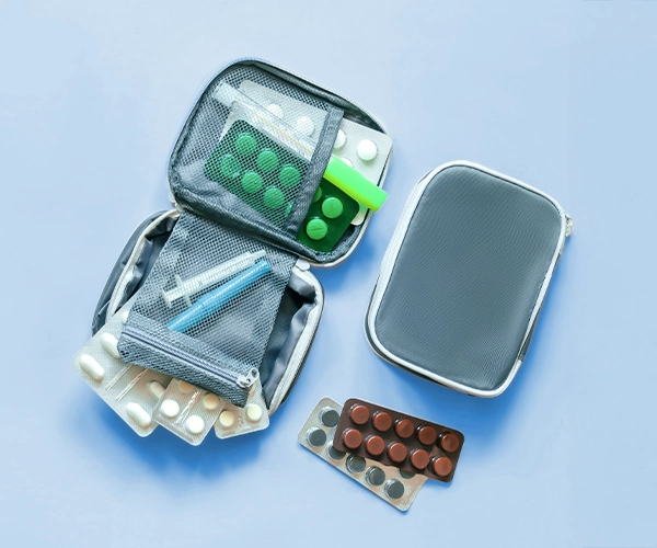 Reisemedikamente Aufgeklappte Reiseapotheke mit Tablettenblistern, Spritzen und Zubehör auf blauem Untergrund – steht für medizinische Vorbereitung auf Reisen.