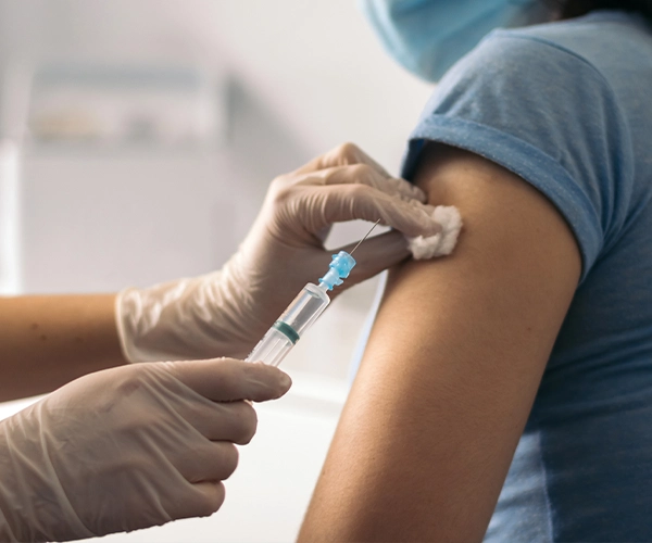 Reisemedizin Nahaufnahme einer medizinischen Fachkraft mit Handschuhen, die einer Person im blauen T-Shirt eine Spritze in den Oberarm verabreicht – symbolisiert Impfung oder Injektion in einer Arztpraxis.