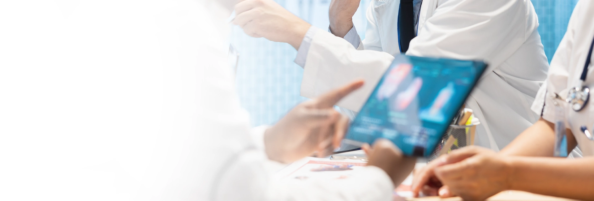 Mehrere Ärztinnen und Ärzte in weißen Kitteln besprechen medizinische Befunde und betrachten gemeinsam digitale Röntgen- oder Bilddaten auf einem Tablet.