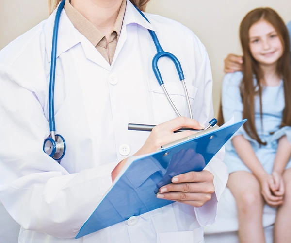 Hausärztin mit Stethoskop hält eine Patientenakte in der Hand, während ein Kind im Hintergrund während der medizinischen Betreuung sitzt.